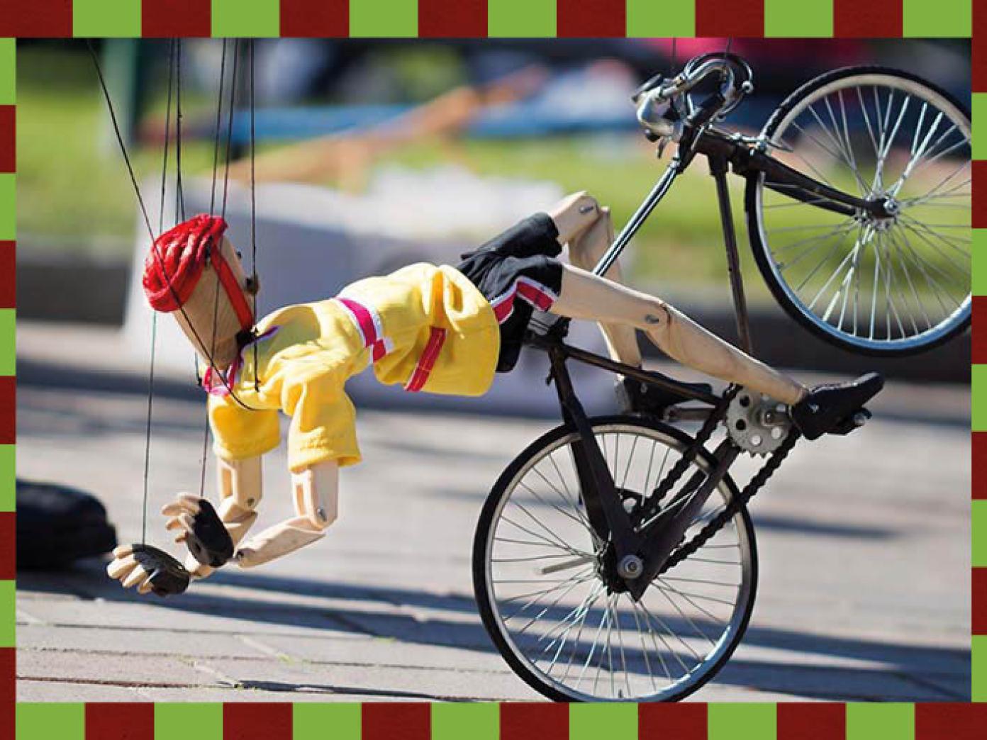 Dukke på dukkecykel på asfalt. Fra 'Hanging by a thread' af Di Filippo Marionette