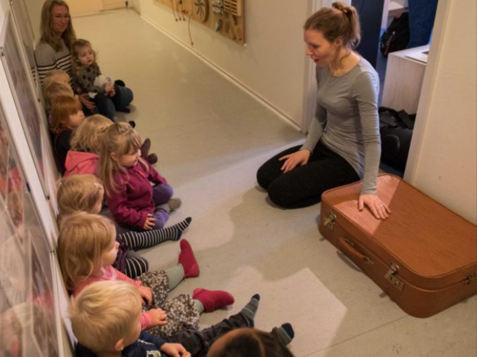Ingrid Tranum Velásquez sidder og fortæller ved siden af en kuffert, imens en masse børn sidder og lytter