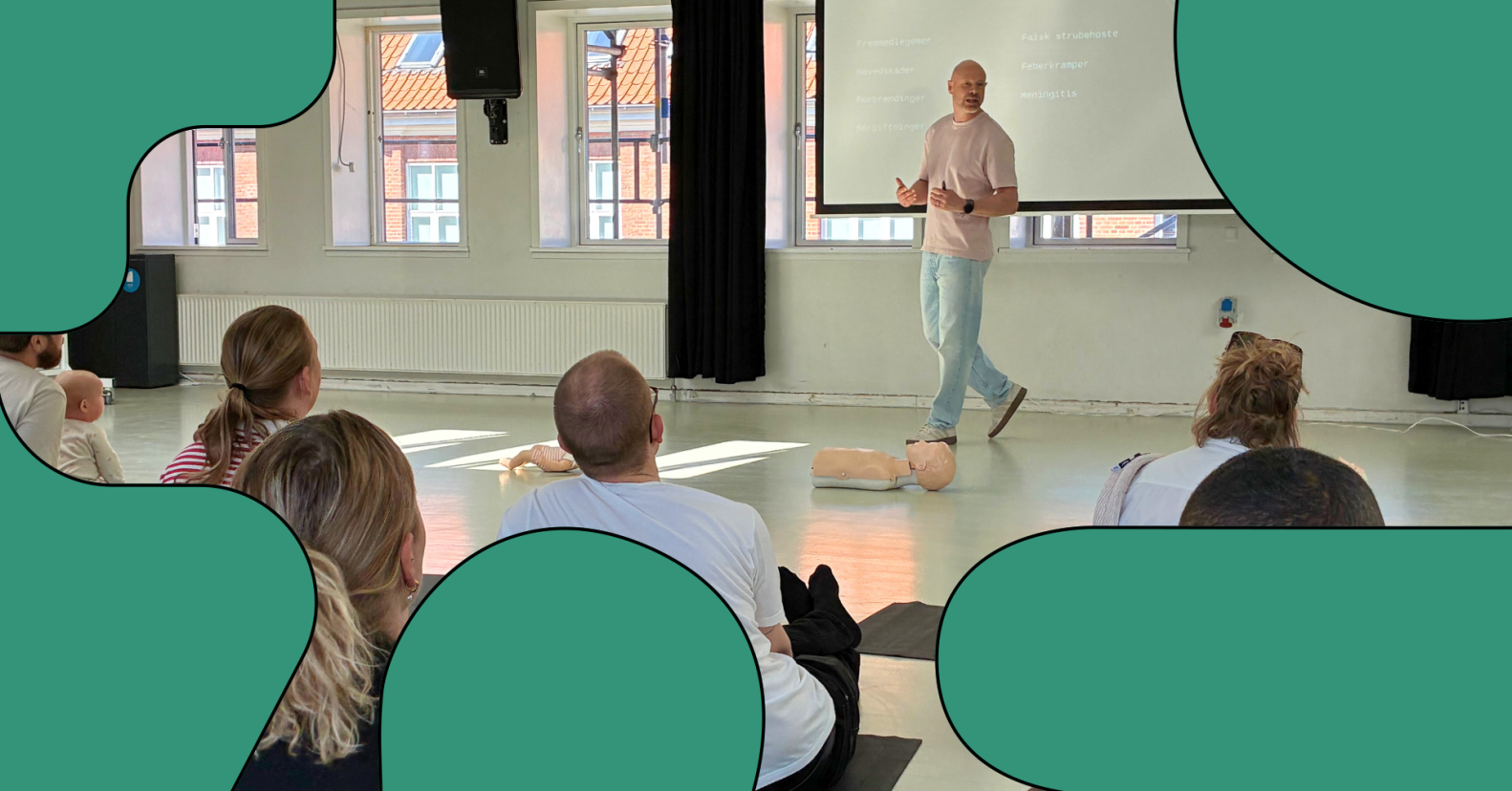 En man underviser en forsamling. På gulvet foran ligger en førstehjælpsdukke